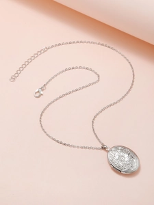 Detailed view of silver oval locket with floral engraving on a pink background