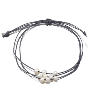 Détail macro du bracelet en cordon gris tressé réglable avec neuf perles baroques blanches