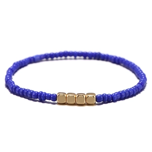 Dettaglio macro del braccialetto di perline blu con quattro cubi metallici dorati centrali