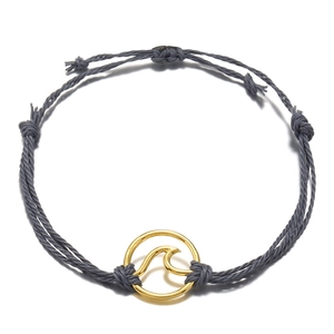 Macro detail of handmade grey braided rope bracelet with golden surf wave charm