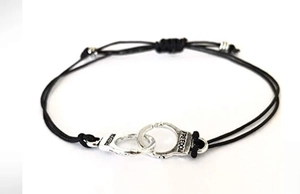 Detail of adjustable black woven cord bracelet featuring silver freedom handcuff charms