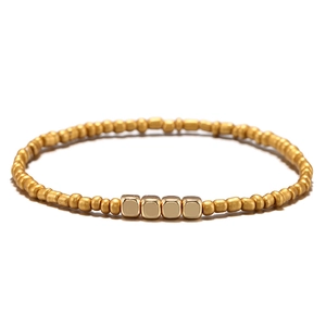 Dettaglio del bracciale con perline dorate e quattro ciondoli quadrati lucidi su bianco