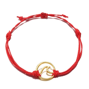 Detail of red handmade braided rope bracelet with a gold circular wave pendant charm