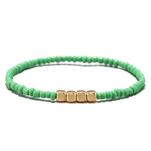 Dettaglio del bracciale bohémien con perline verde smeraldo e cubi dorati su sfondo bianco