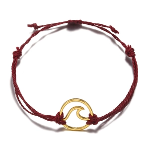 Detail of red woven beach bracelet with a golden circular wave charm in minimalist style
