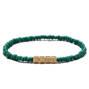 Dettaglio ravvicinato di un bracciale di perline verdi con quattro cubi in metallo oro