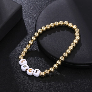 Detailed close-up of golden beaded bracelet with LUCK acrylic letter beads on dark background