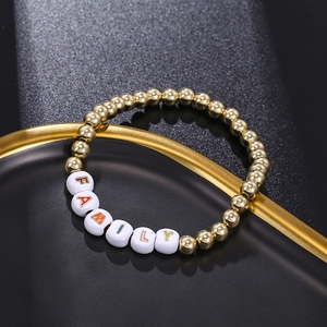 Detailed close-up of golden beaded bracelet with white square cubes spelling FAMILY