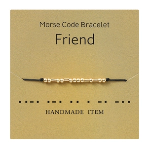 Close-up of Morse code friendship bracelet with gold beads on a branded display card