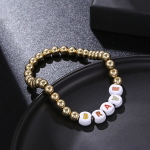 Detailed shot of golden beaded bracelet with colorful letters spelling BRAVE on a black plate