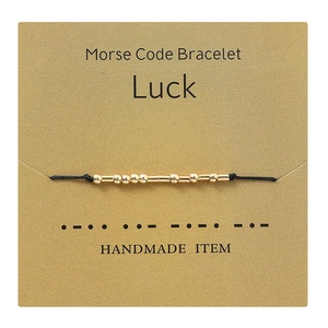 Detail of handmade Morse code bracelet with gold beads on a Luck message card