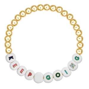Macro detail of beaded bracelet with golden beads and white Keep Going letter charms