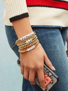 Detail of layered gold beaded bracelets with white letter beads featuring courage and love