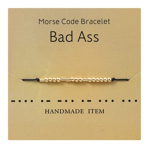 Detail of handmade gold Morse code bracelet on textured gift card with letter coding