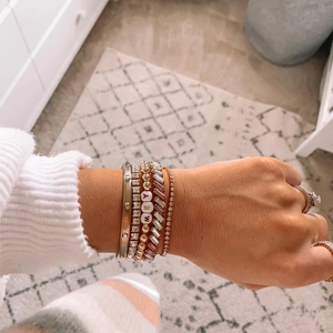 Close-up of stacked gold and silver bracelets with letter beads and zircon rings