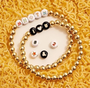 Macro detail of custom gold beaded stretch bracelets with acrylic alphabet letter beads