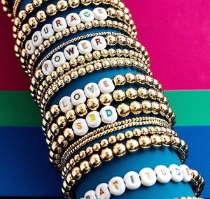 Detail of gold beaded bracelets featuring letter beads with Courage, Power, and Love words