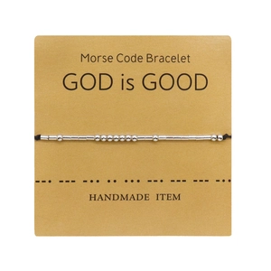 Detalle de pulsera con código Morse en cartón kraft con cuentas y texto GOD is GOOD