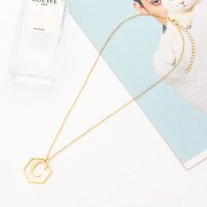 Golden hexagonal letter C pendant necklace on white surface with luxury perfume bottle