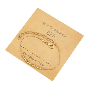 Dettaglio del braccialetto Morse Code BFF dorato su cartoncino kraft con testo fatto a mano