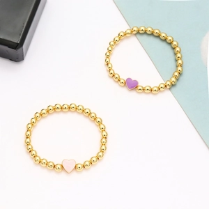 Dettaglio dei bracciali con perline dorate e ciondoli a cuore in smalto rosa e viola