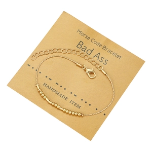 Dettaglio del bracciale in codice Morse dorato con perline e tubi su cartoncino