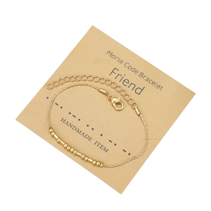 Dettaglio del bracciale Morse dorato su cartoncino kraft con chiusura a moschettone