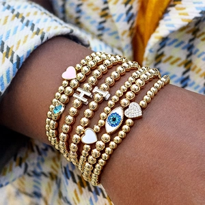Dettaglio del bracciale dorato a strati con ciondoli a cuore e occhio di Allah