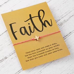 Bracciale a croce in corda rosa intrecciata su biglietto Faith con sfondo in legno bianco