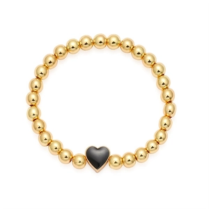 Bracciale a sfere dorate con ciondolo a cuore nero minimalista su sfondo bianco