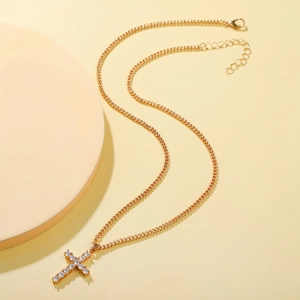 Elegant gold cross necklace with crystal pendant on a minimalist round display stand