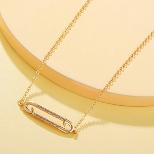 Detail of gold safety pin pendant with inlaid cubic zirconia on a minimalist chain