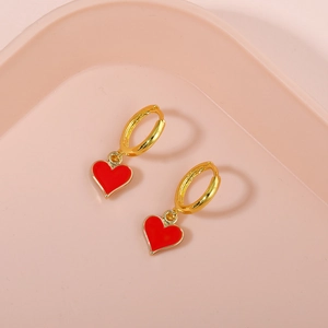 Close-up of golden geometric earrings featuring vibrant red enamel heart charms