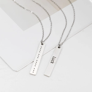 Close-up of polished stainless steel bar pendants with Luck text and Morse code engraving