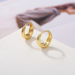 Detailed close-up of polished gold-plated huggie earrings on a minimalist display