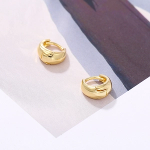 Detail view of polished gold-plated huggie earrings with a sleek minimalist round design