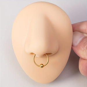 Close-up of a golden captive bead ring worn on a silicone nose model for piercing display