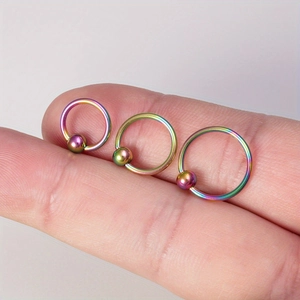 Macro view of three rainbow stainless steel captive bead rings held on fingertips