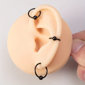 Three-piece set of black stainless steel captive bead rings on a silicone ear model