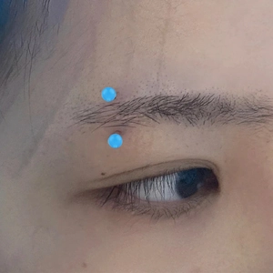 Close-up view of a blue acrylic curved barbell eyebrow piercing worn on the face