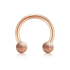 Makroaufnahme von roségoldenem Hufeisen-Piercing mit mattierten Glitzerkugeln auf Weiß