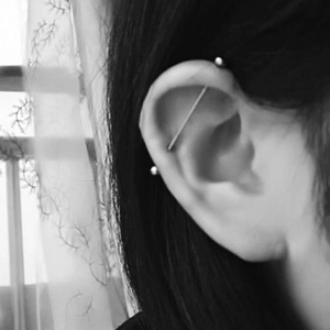 Black and white close-up of a stainless steel industrial barbell piercing on the ear