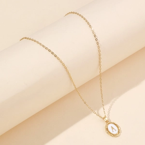 Vue détaillée du pendentif lettre A dorée avec émail blanc sur un support minimaliste