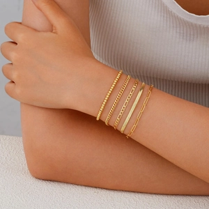 Detailansicht eines goldenen Armband-Sets mit Panzer- und Büroklammerkette am Handgelenk