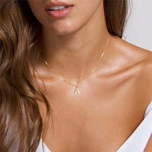 Detail of a minimalist gold necklace with a capital letter A pendant on a thin chain