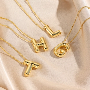 3D balloon initial pendant necklaces in gold finish on champagne silk background