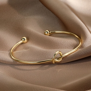 Polished 14k gold plated knot open cuff bracelet on elegant silk background