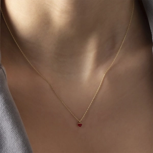 Close-up of a minimalist gold necklace with a delicate red heart pendant on model