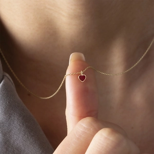 Close-up of mini red heart pendant necklace on finger showing delicate golden chain