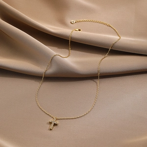Detail of gold cross necklace with crystal pavé on dark brown pleated silk fabric